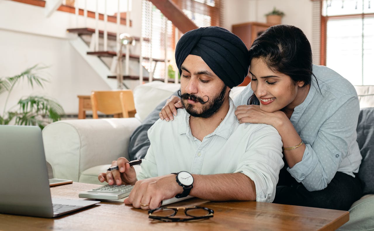 Smiling couple collaborating at home with a laptop and calculator, fostering teamwork.